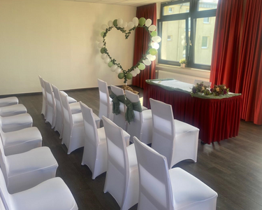 Reihen von Stühlen mit weißen Hussen vor einem Tisch, daneben ein großes Herz aus Blumen